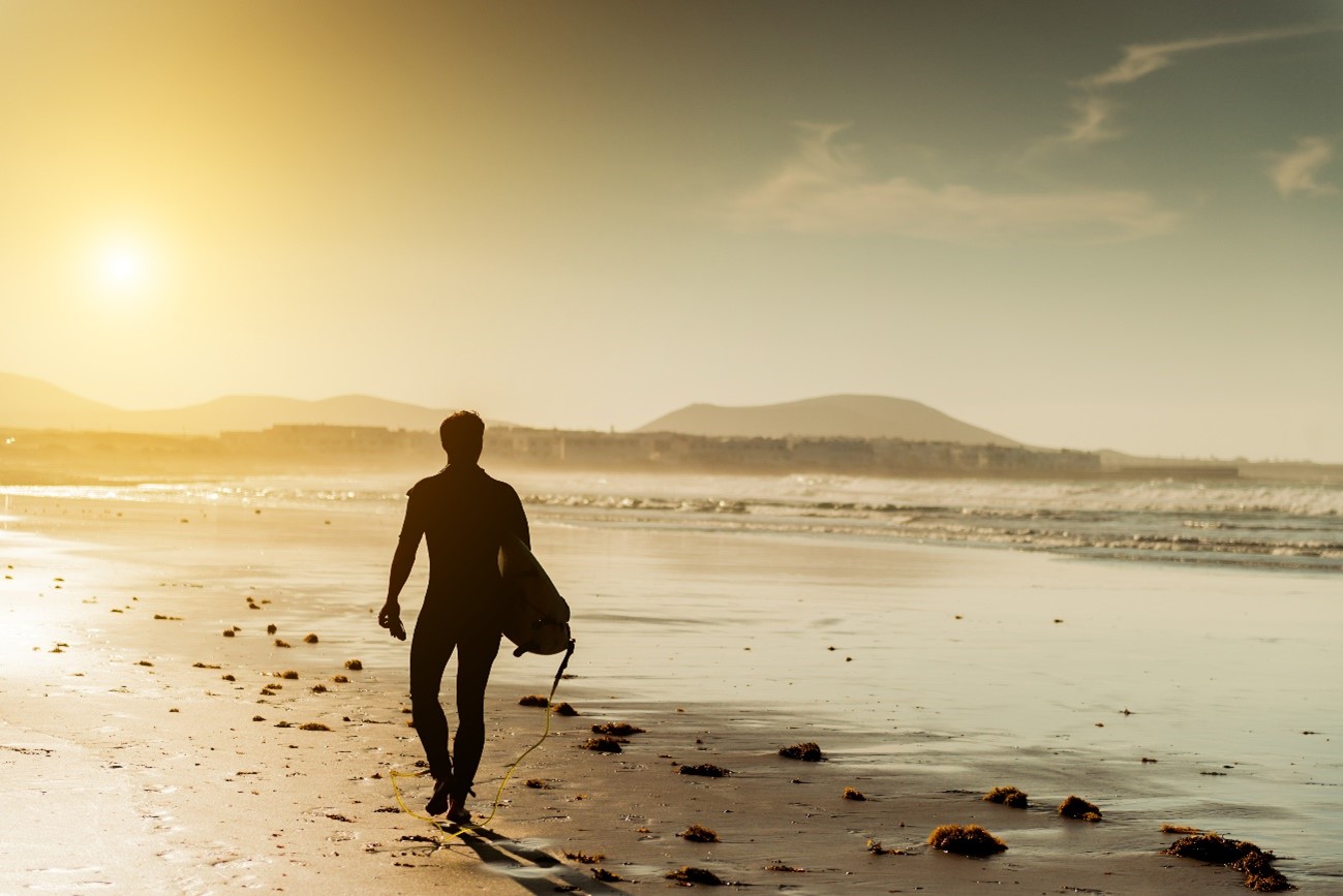 Un surfista camina hacia la orilla en una playa de arena blanca en Canarias